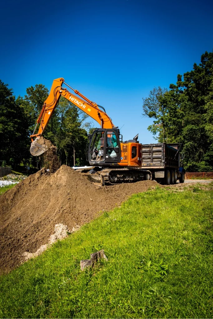 An excavation contractor is operating an orange excavator on a pile of dirt.