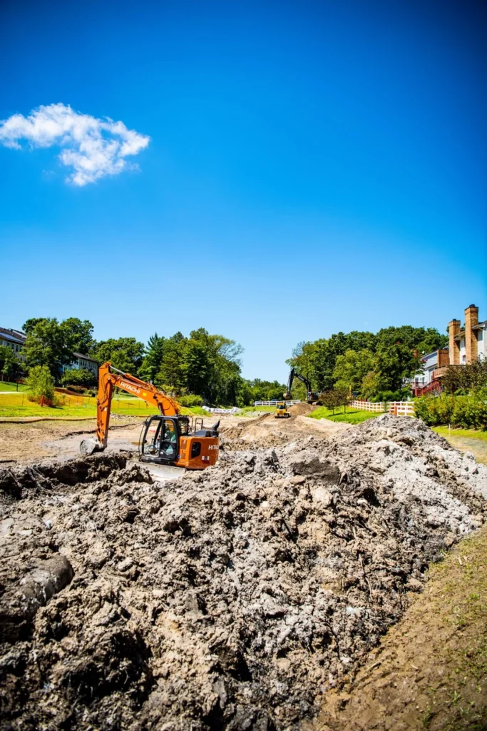 An excavator is performing earthwork for site development by digging a hole in the ground.