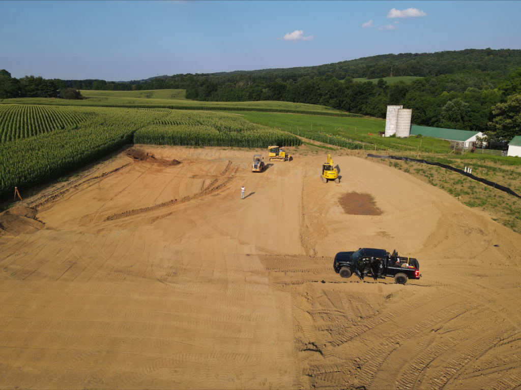 An site development contractor utilizes a tractor and a bulldozer for stormwater management in an aerial view of a dirt field.