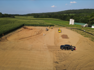 An earthwork contractor utilizes a tractor and a bulldozer for stormwater management in an aerial view of a dirt field.