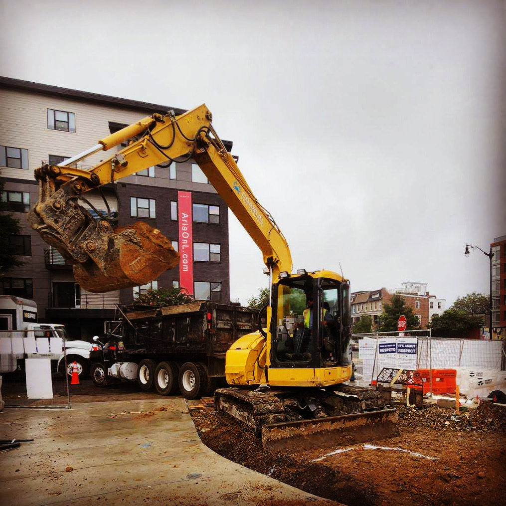 A yellow excavator performing site development on a construction site.