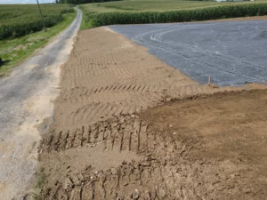 An excavation contractor prepares a dirt road for site development, incorporating stormwater management solutions with the addition of a tarp in the middle.