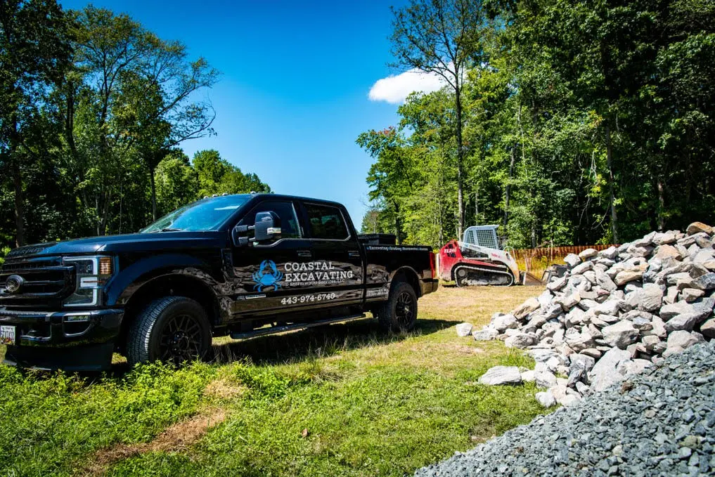 A black truck is parked in front of a pile of rocks during site development.