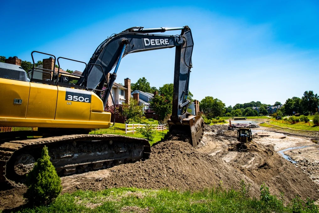 An excavation contractor is using a yellow excavator for site development on a dirt road.