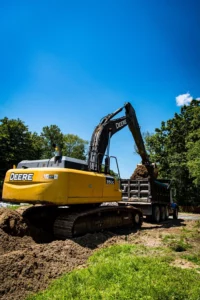 A excavation contractor is using a yellow excavator for site development by digging a hole in the dirt for stormwater management.